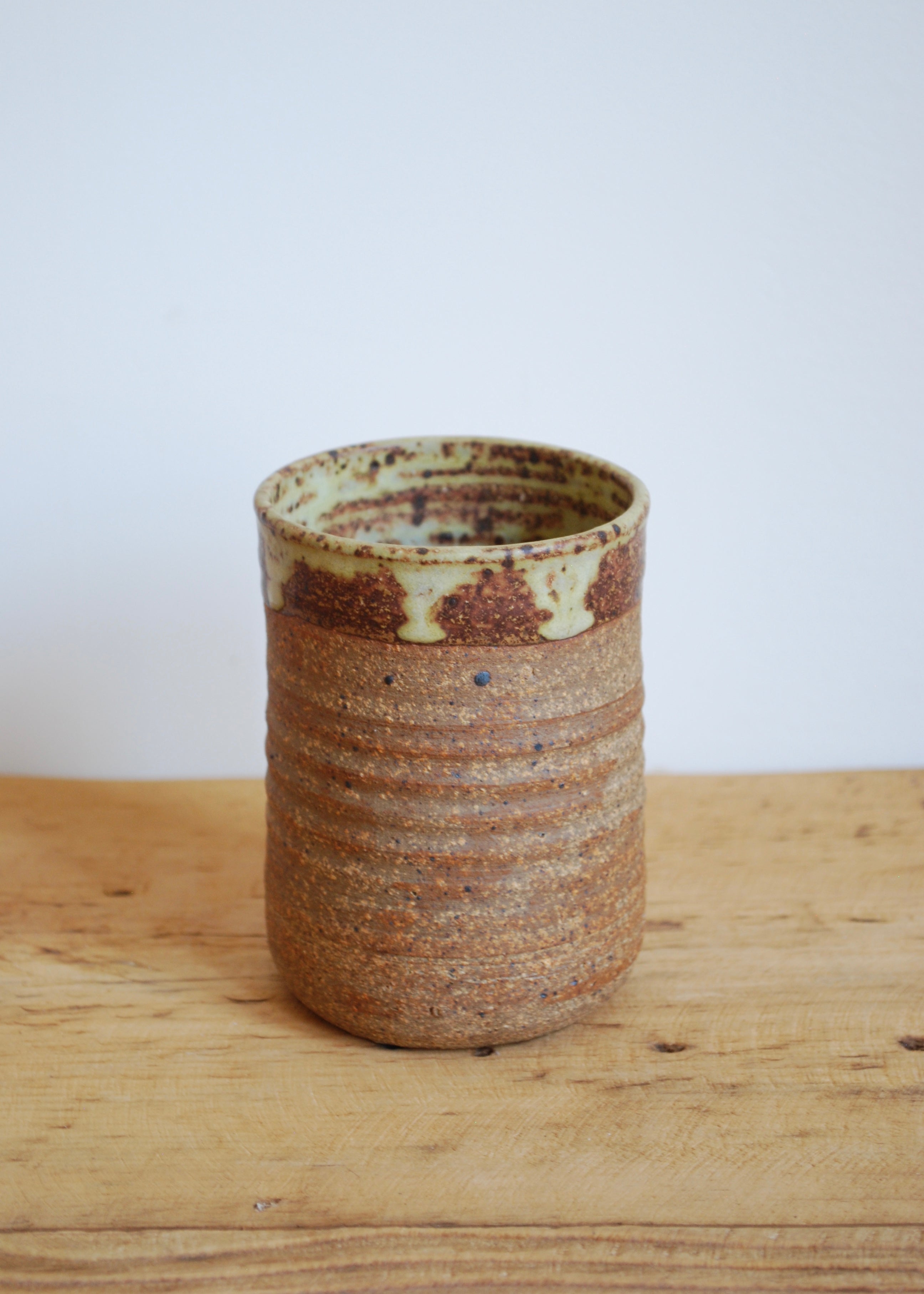 Handmade ceramic cup with brown and beige glaze on a wooden surface