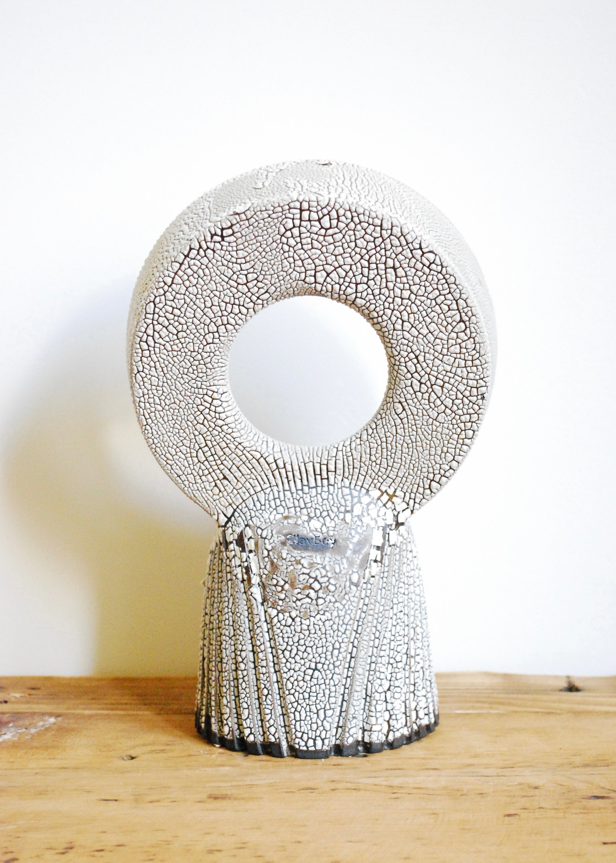 A handmade circular ceramic object with textural cracked white glaze