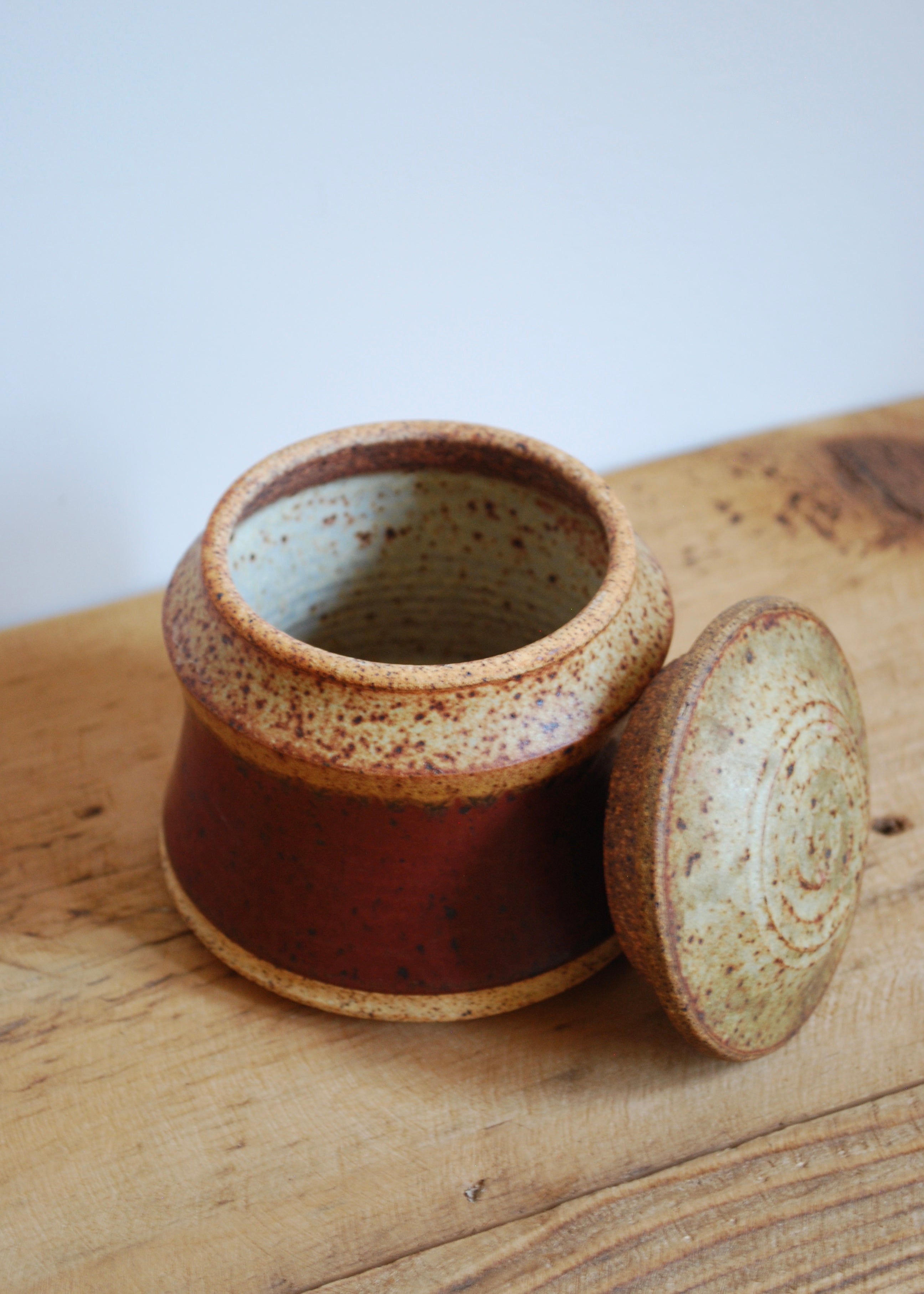 Speckled brown ceramic jar with lid on a wooden surface