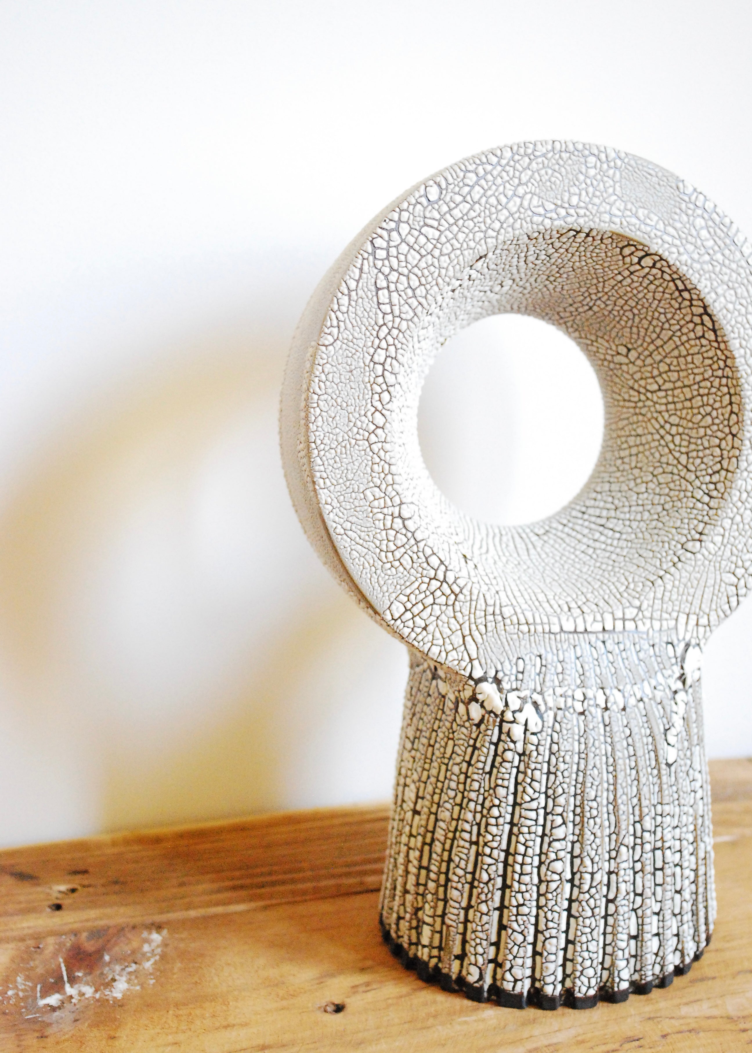 A handmade circular ceramic object with textural cracked white glaze