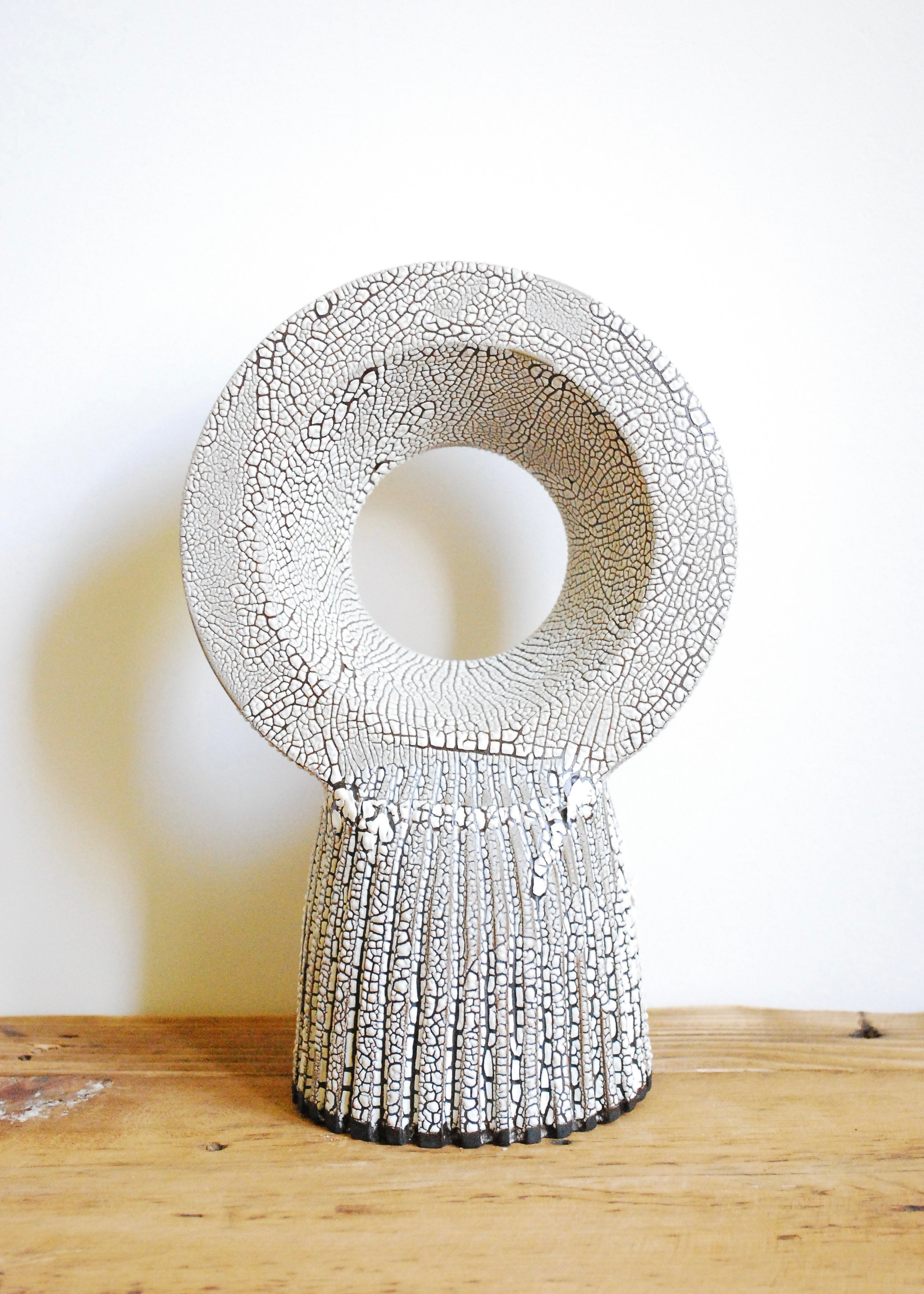 A handmade circular ceramic object with textural cracked white glaze
