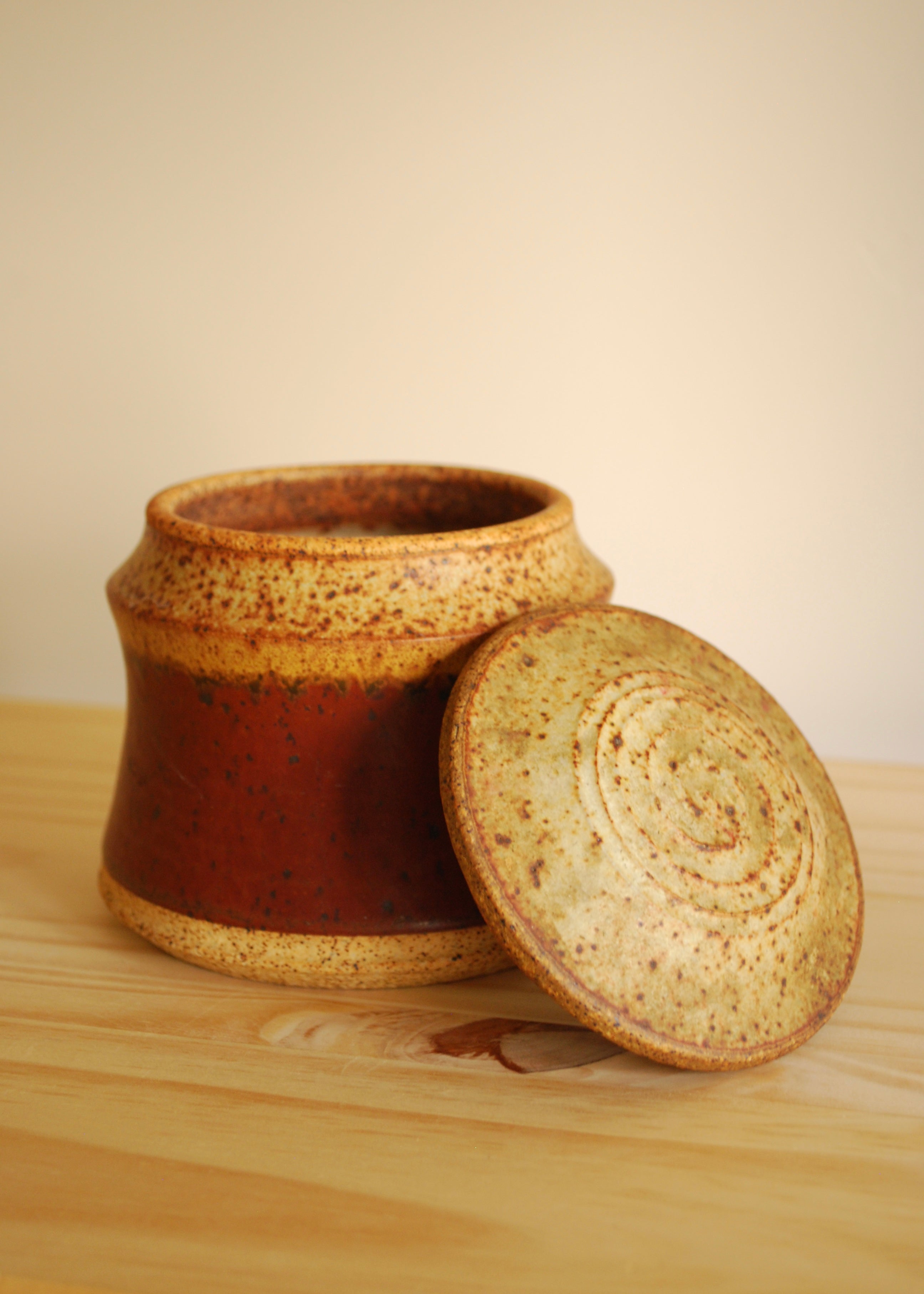 Red and beige ceramic jar with a lid on a wooden surface