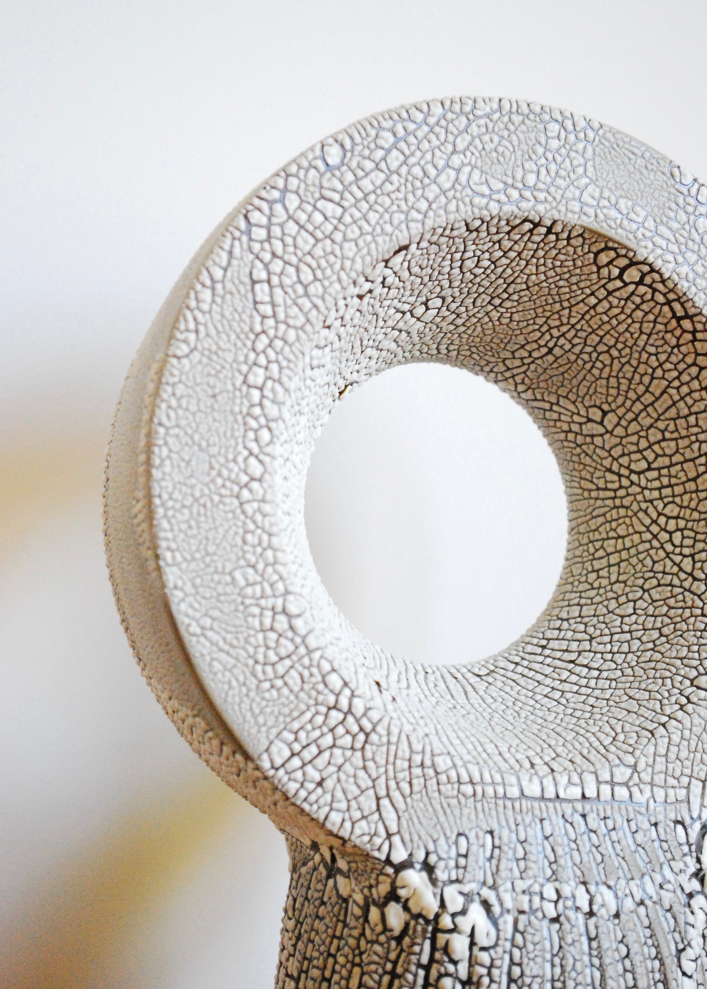 A handmade circular ceramic object with textural cracked white glaze 