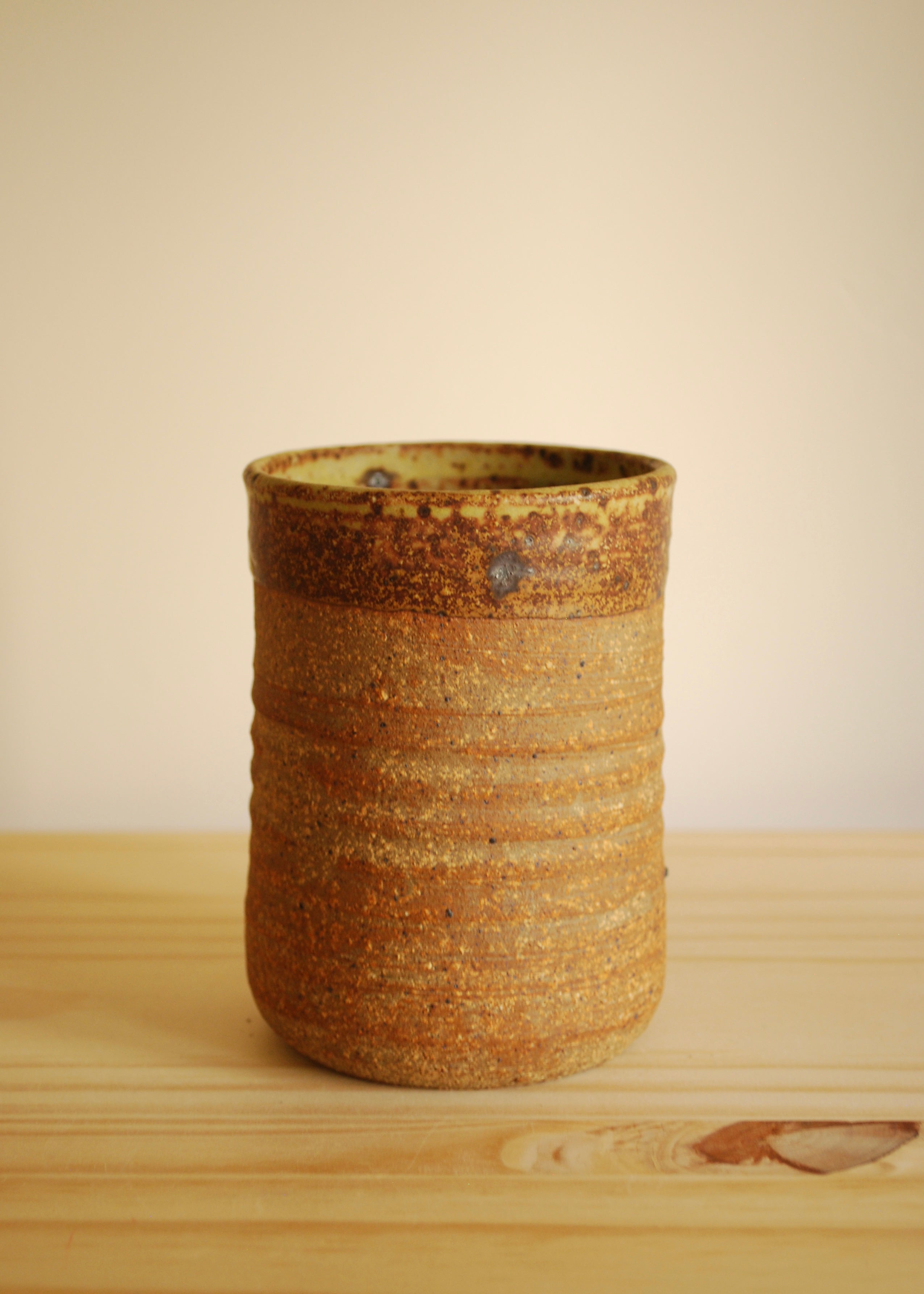 Handmade ceramic cup with brown and beige glaze on a wooden surface