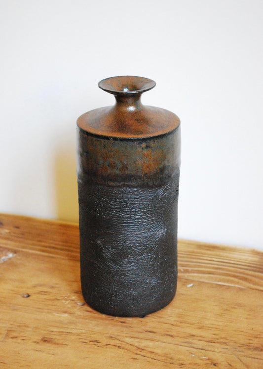 Tall handmade ceramic vase in black clay with texture around the body and and ancient iron brown glaze at top and spout 