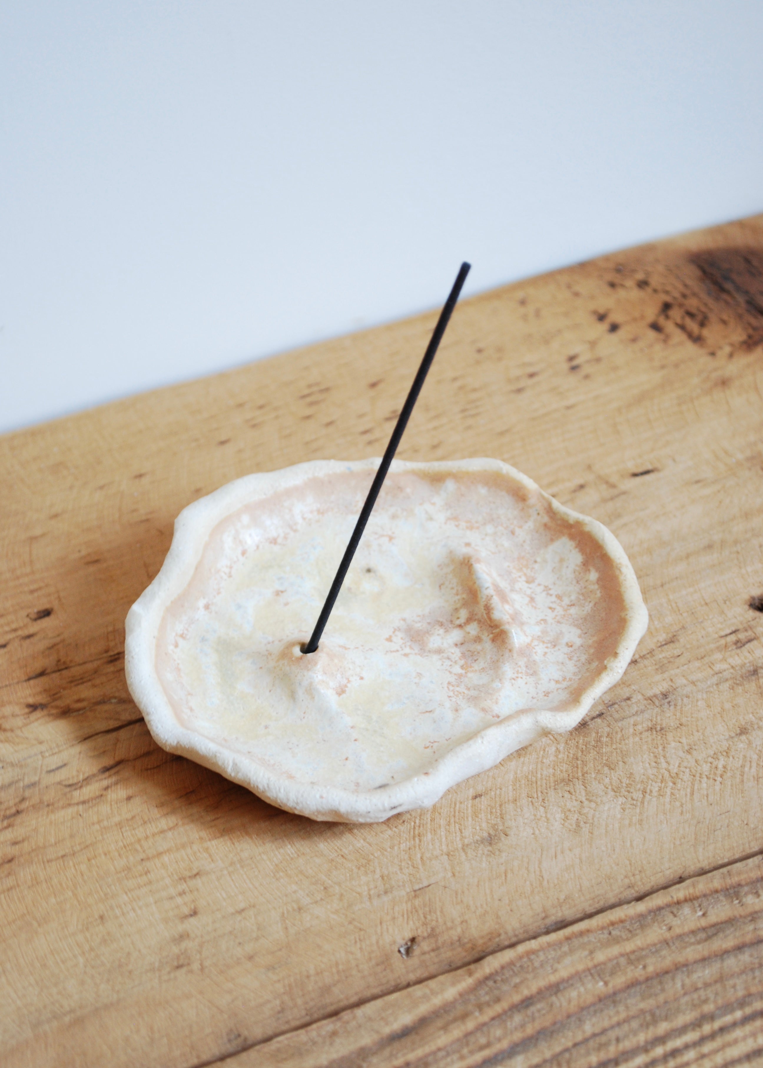 Handmade beige ceramic incense tray on a wooden platform 
