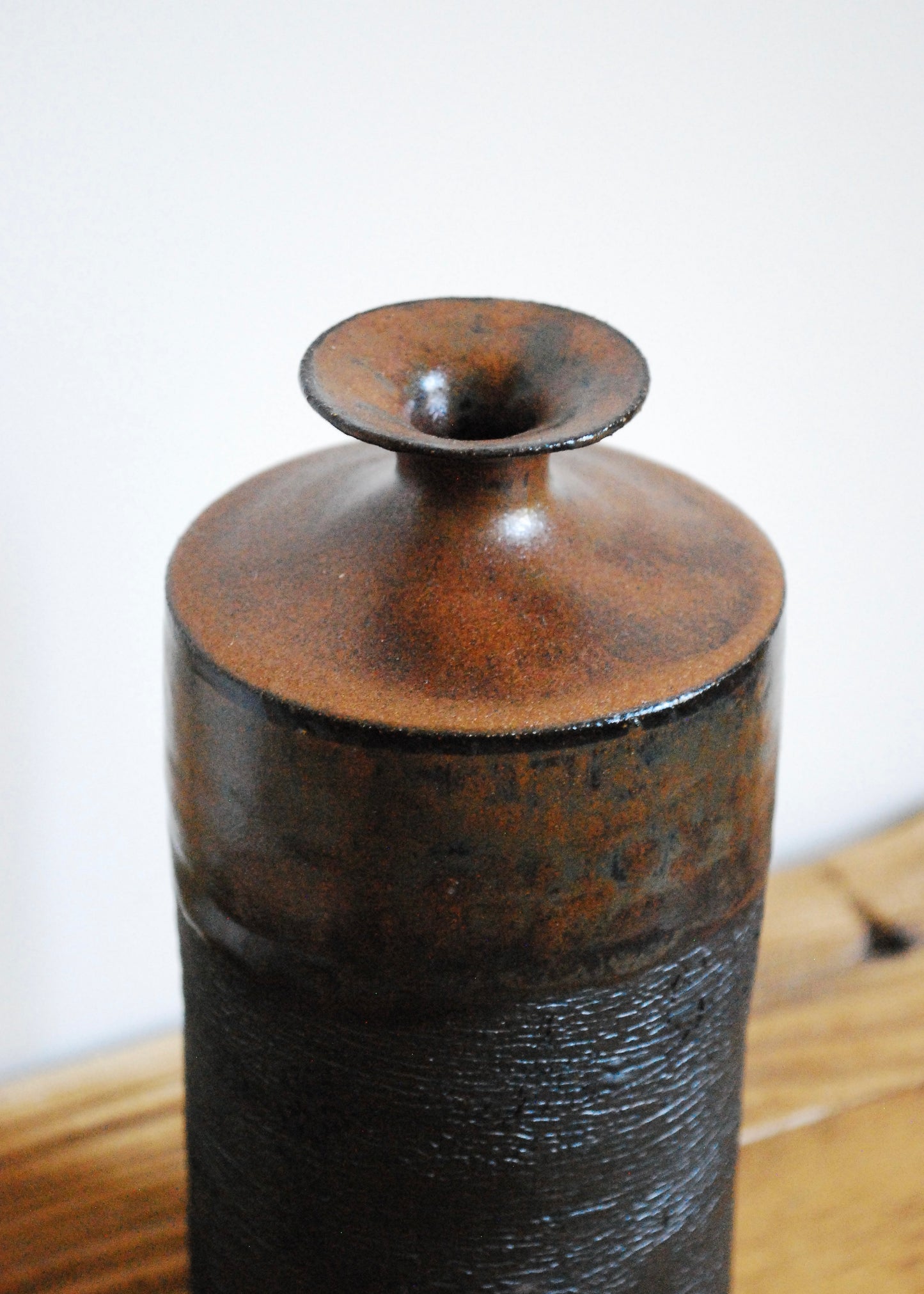 Tall handmade ceramic vase in black clay with texture around the body and and ancient iron brown glaze at top and spout 