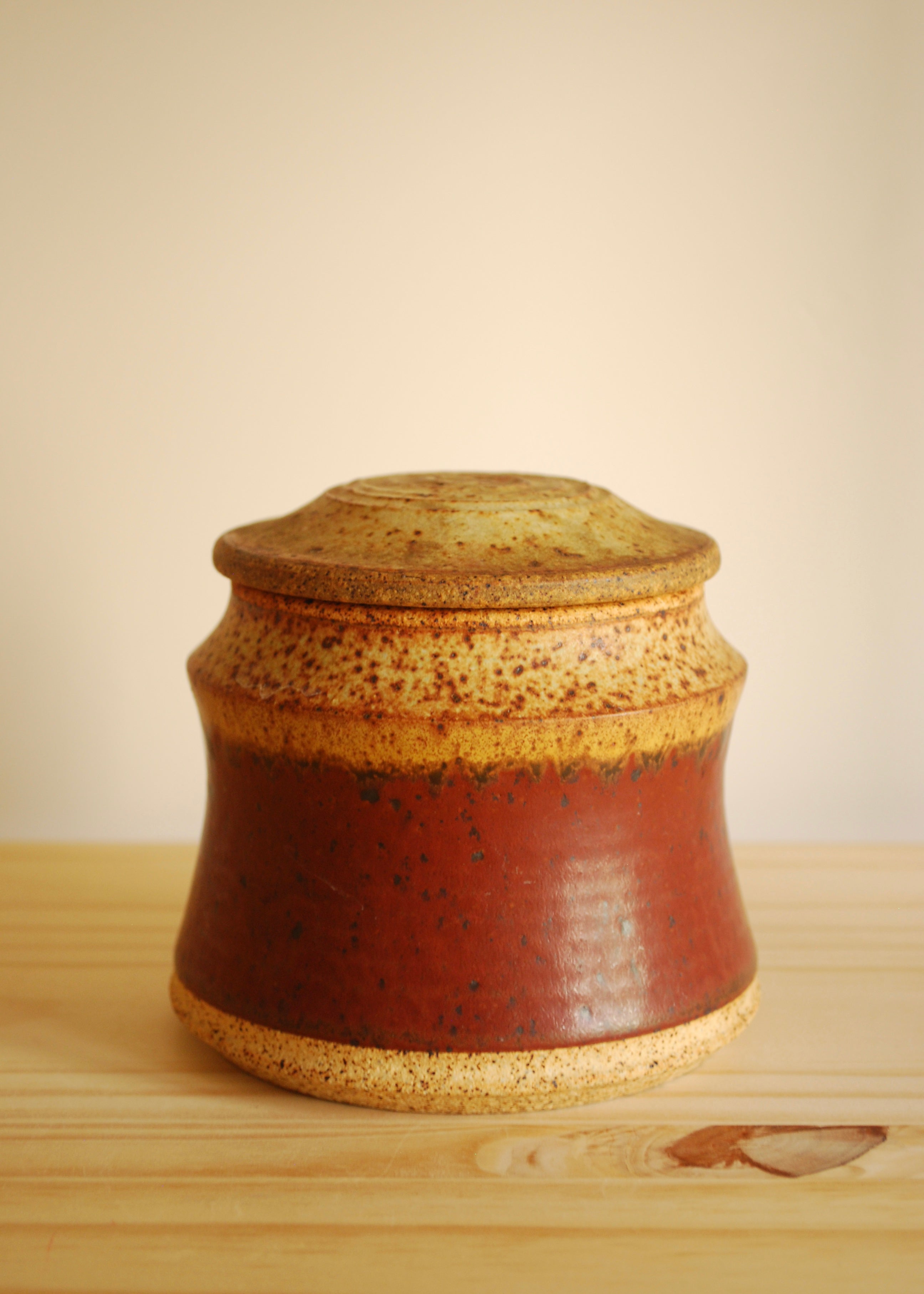 Red and beige ceramic jar with a lid on a wooden surface