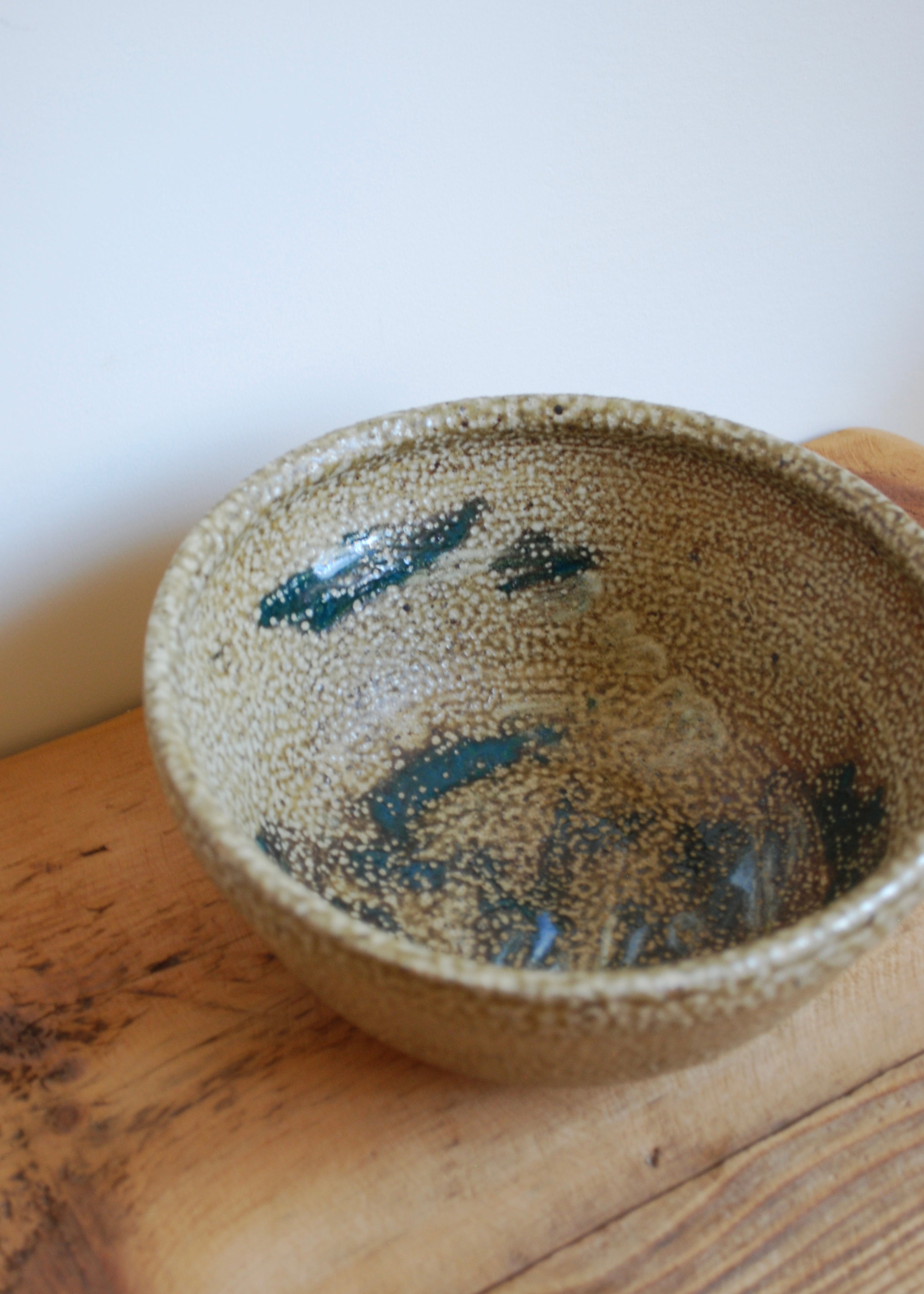 Ceramic studio bowl with speckled glaze on a wooden surface