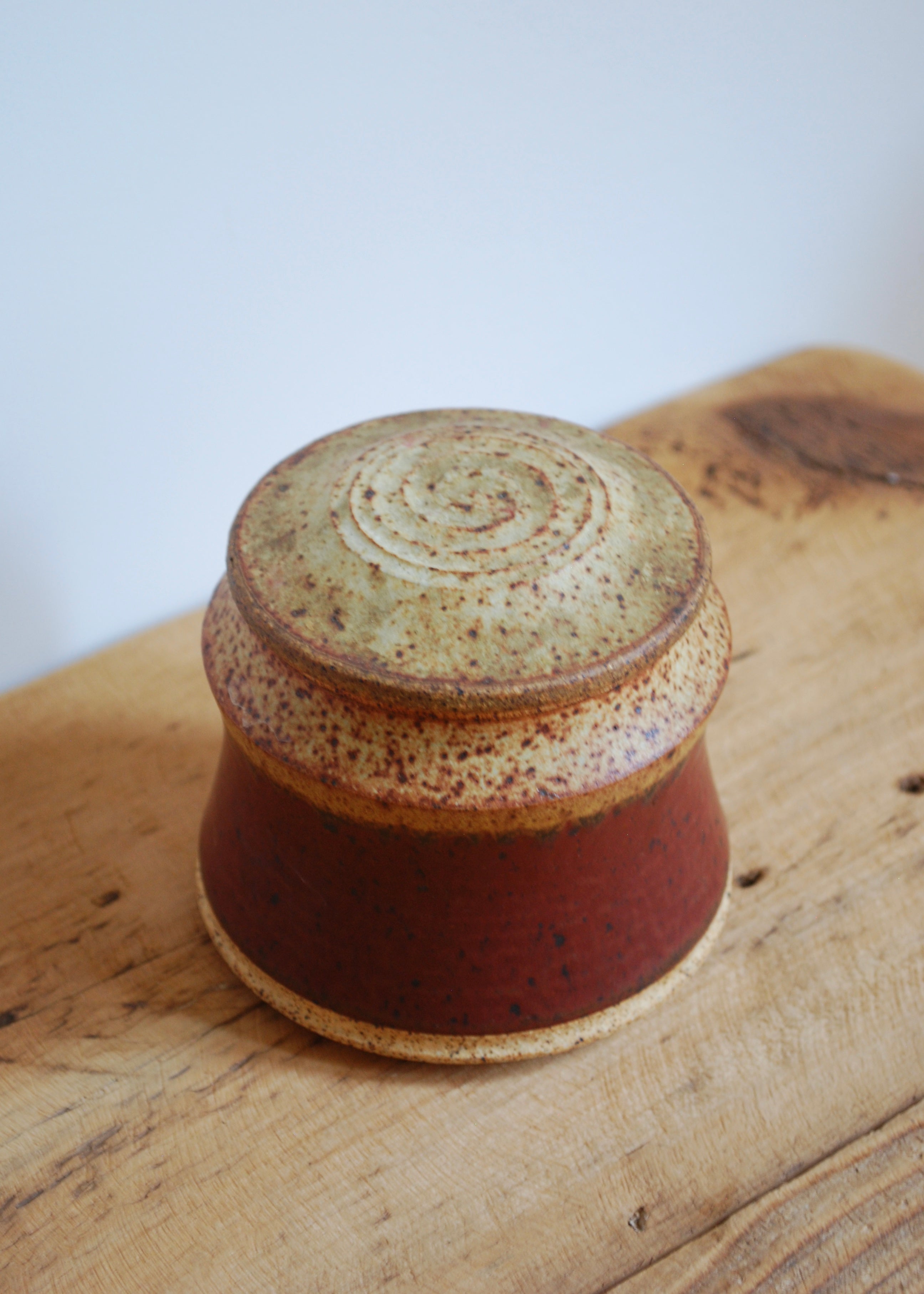 Red and beige ceramic jar with a lid on a wooden surface
