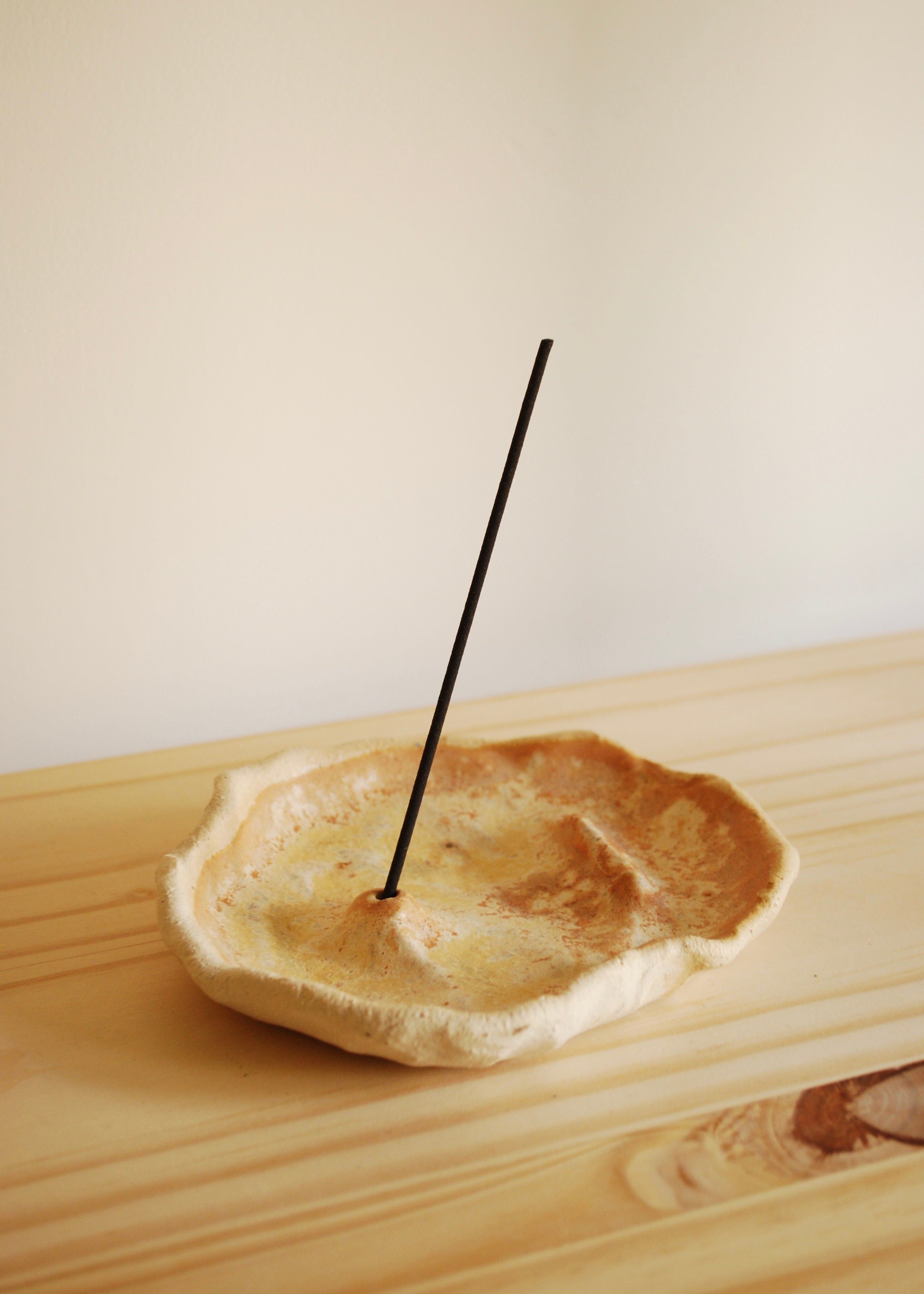 Handmade beige ceramic incense tray on a wooden platform 
