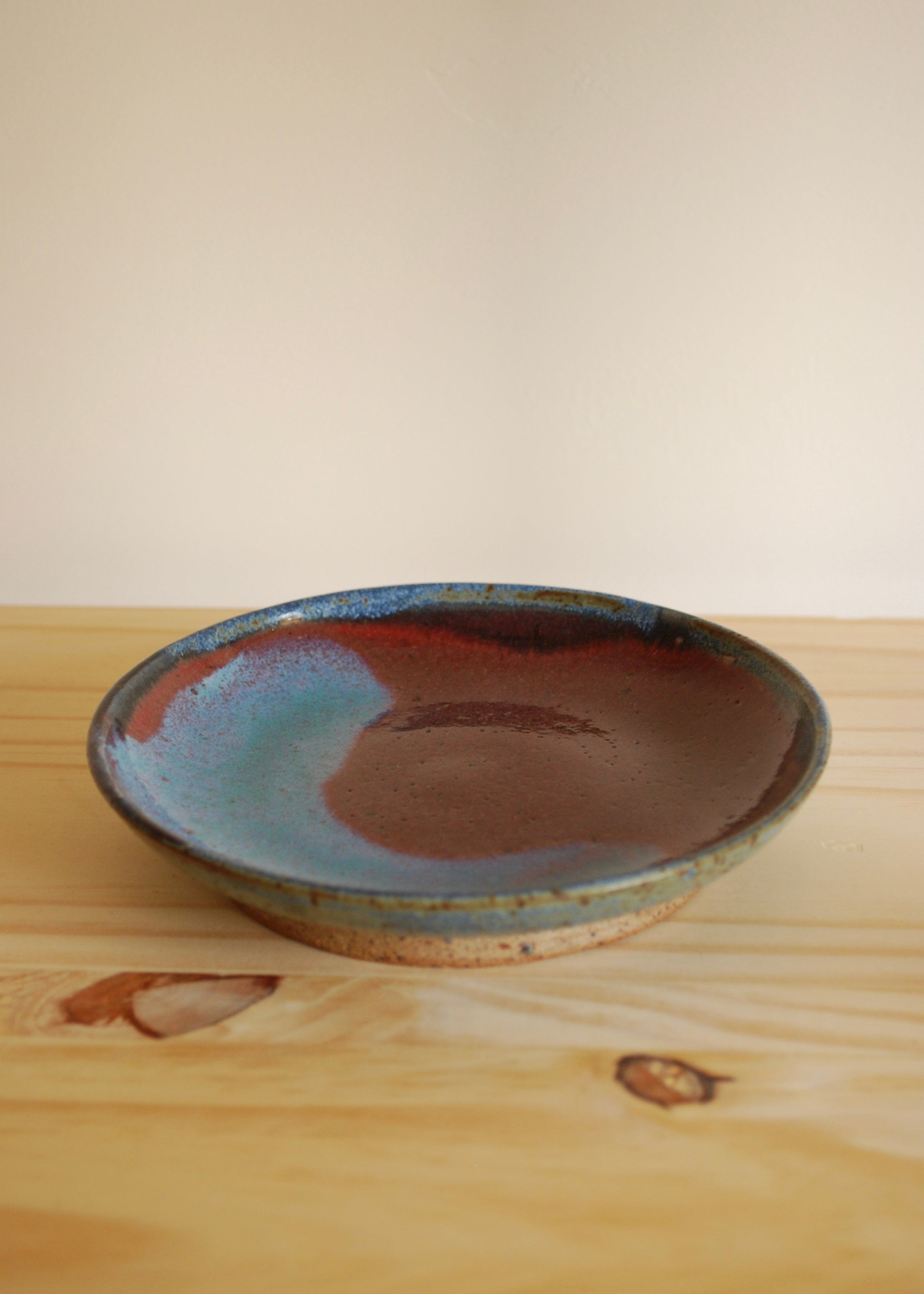 Handmade ceramic plate with a blue and brown glaze on a wooden surface