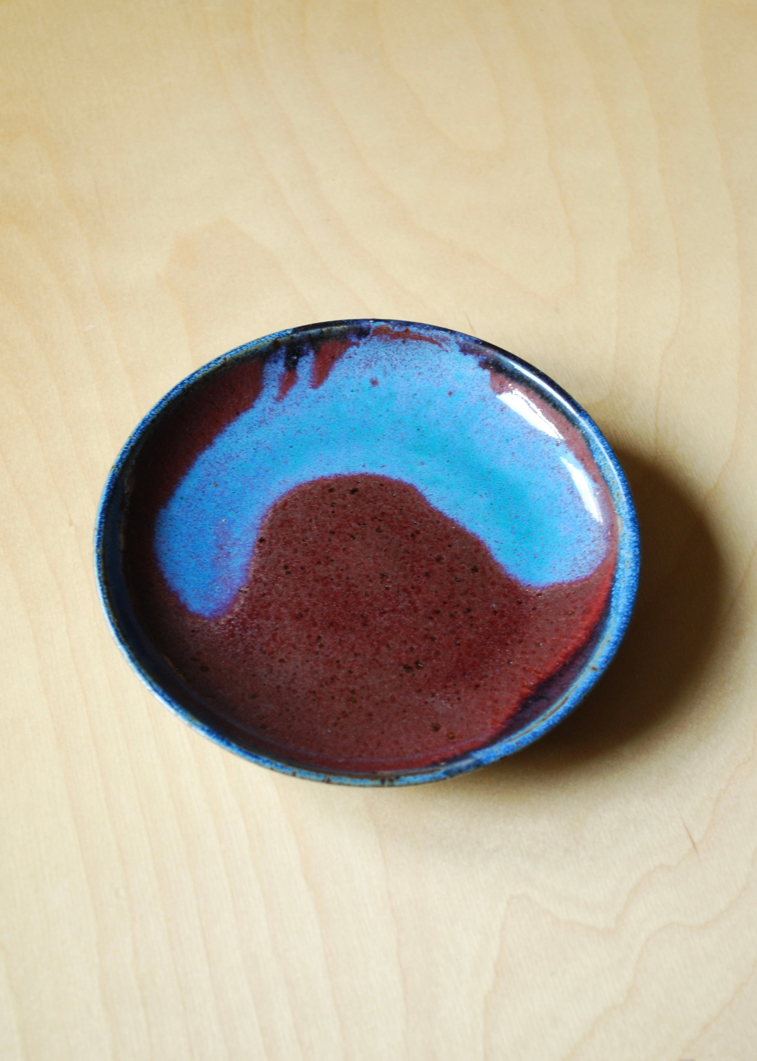 Handmade ceramic dish with blue and brown glaze on a beige surface