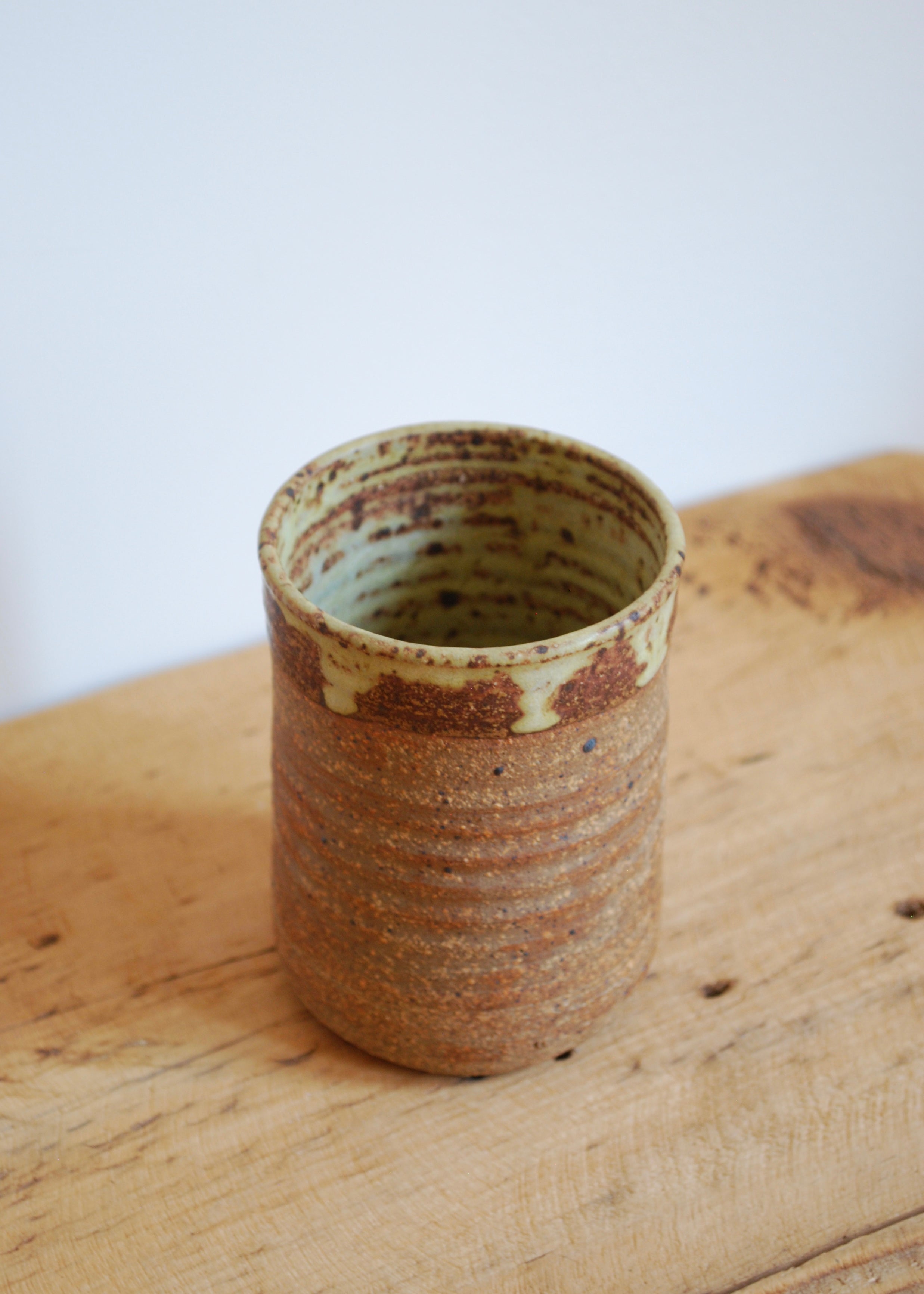 Handmade ceramic cup with brown and beige glaze on a wooden surface